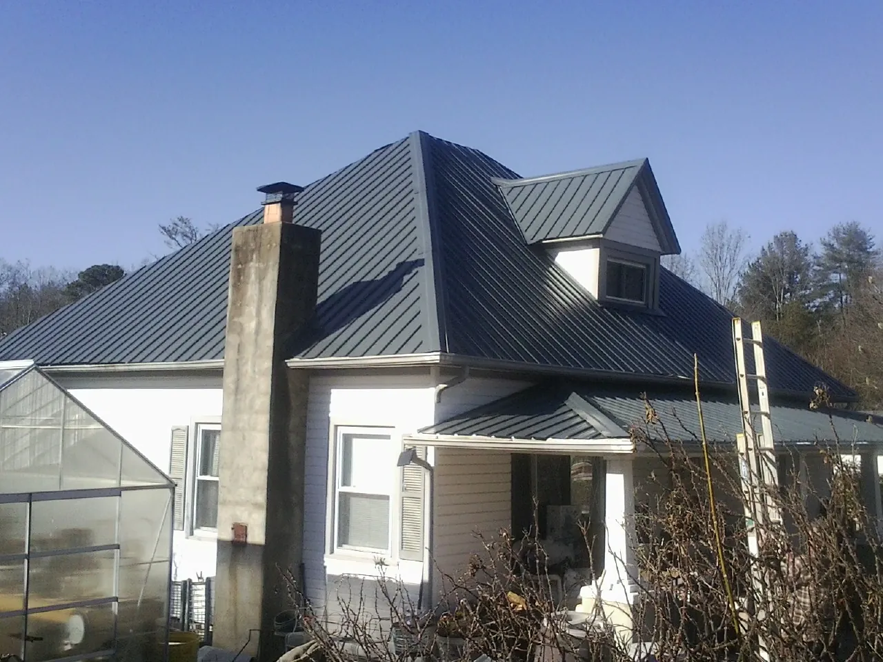 Dark blue standing seam metal roof on a white farmhouse with dormer — Slate & Tile Roof Repair by Roofing Brothers in Sedalia